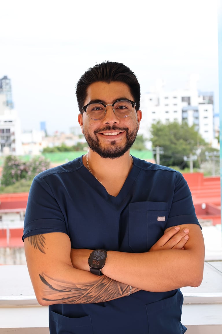 Man with tattoos and beard wearing glasses and dark blue shirt, smiling with arms crossed in front of city skyline